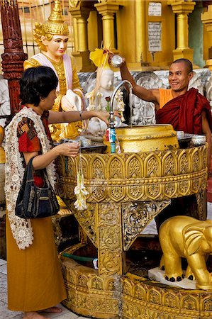 Myanmar,Burma,Yangon. A Buddhist monk and a worshipper anoint a statue of Buddha at a shrine in the Shwedagon Golden Temple complex. Stock Photo - Rights-Managed, Code: 862-03365087