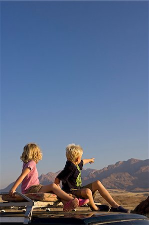 Namibia,Damaraland. With Brandberg Mountain Namibia's highest peak in the background two young children go game viewing from the top of a four wheel drive in late afternoon light. Stock Photo - Rights-Managed, Code: 862-03365355