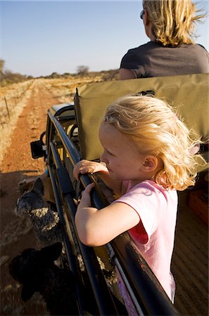 simsearch:862-03713630,k - Région de Erongo Damaraland, Namibie. Une jeune fille, ses cheveux soufflant dans le vent, se penche sur le côté d'un véhicule de safari comme il pousse dans des pâturages sur une piste de jeu Photographie de stock - Rights-Managed, Code: 862-03365388