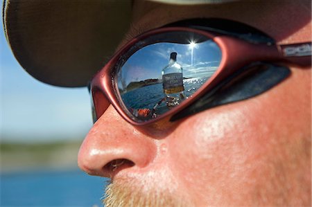 Norway,Nordland,Helgeland. Looking out over the coastal waters near the town of Bodo- a bottle of whisky reflected in the Norwegian tour guide's mirrored sunglasses Stock Photo - Rights-Managed, Code: 862-03365690