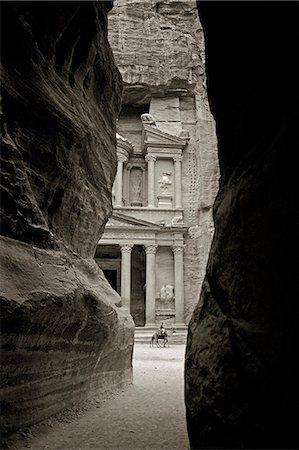 A boy leads a group of camels past the ancient facade of the Khazneh (Treasury),as viewed through the Siq. The Khazneh is forty metres high and is thought to have been hewn from the sandstone walls by the Nabataeans between 100 BC and 200 AD. Foto de stock - Direito Controlado, Número: 862-03365837