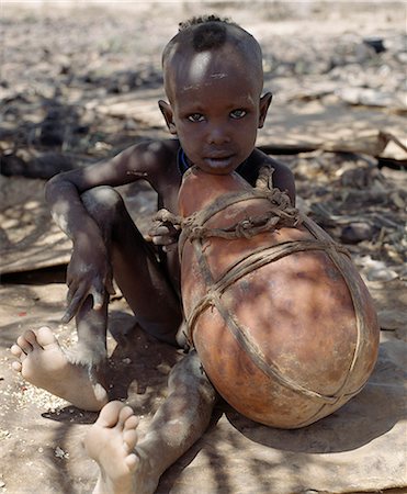 A young Turkana boy looks pensive as he holds a large gourd. Gourds are less common with the Turkana than the wooden containers their women make; firstly,they are expensive since they have to be brought from afar but more importantly they crack more easily on the move. Stock Photo - Rights-Managed, Code: 862-03366123