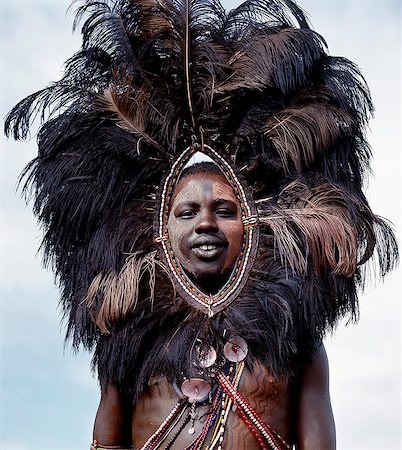 A Maasai warrior,his face and body decorated with red ochre and clay,wears an ostrich feather headdress. This singular adornment was once worn by warriors going into battle and was likely designed to frighten an enemy. Foto de stock - Con derechos protegidos, Código: 862-03366154