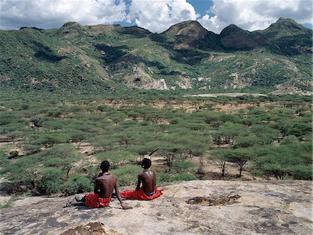 Two Samburu warriors relax on a rock outcrop near the foothills of the Ndoto Mountains in Samburuland. This northern region of semi-arid thorn scrub country barely supports sufficient livestock for the semi-nomadic pastoralists living there.The Samburu of Northern Kenya are related to their more famous cousins,the maa speaking Maasai. Stock Photo - Rights-Managed, Code: 862-03366416