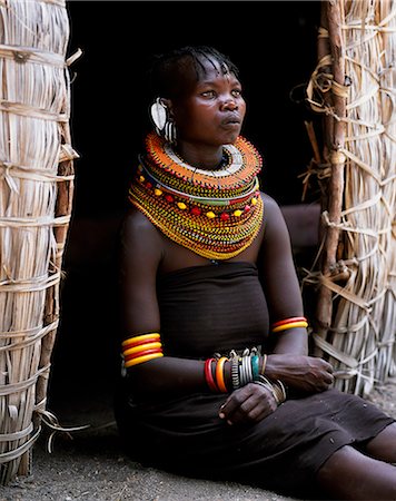 simsearch:862-03820429,k - Une femme de Turkana, généralement porter plusieurs épaisseurs de colliers de perles et une série de boucles d'oreilles arceau avec une paire d'earrrings en forme de feuille sur le devant, se trouve dans l'entrée de sa hutte. Photographie de stock - Rights-Managed, Code: 862-03366495