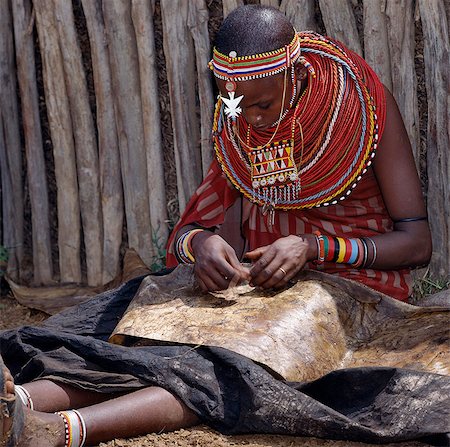 A Samburu woman sews a leather cloak for her younger brother. For several weeks before a boy is circumcised,he must wear a charcoal-blackened cloak,which is made from three goatskins. Stock Photo - Rights-Managed, Code: 862-03366539