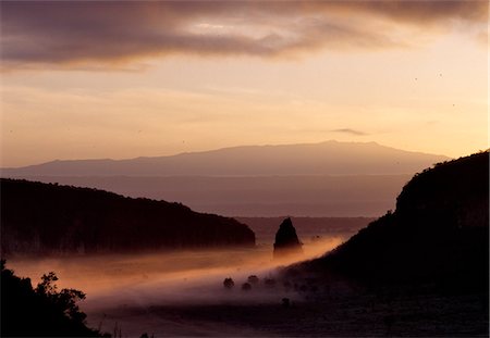 Early morning ground mist surrounds Fischer's Tower,an ancient volcanic plug,in a region of Kenya where the latent signs of volcanic activity are still evident. The Aberdare Mountains rise in the far distance. The tower was named after a German explorer,Gustav Fischer,who was the first European to reach the area in 1883. Stock Photo - Rights-Managed, Code: 862-03366593