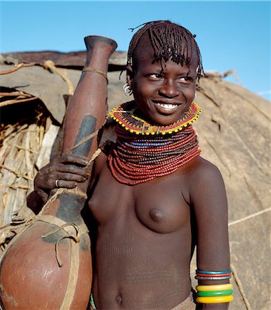 simsearch:400-05021263,k - A Turkana girl with a large gourd-like container used as a receptacle for water or milk. In the absence of gourds,the Turkana carve their containers from soft wood,such as that from the common commiphora species,which thrives in semi-arid country. Foto de stock - Con derechos protegidos, Código: 862-03366607