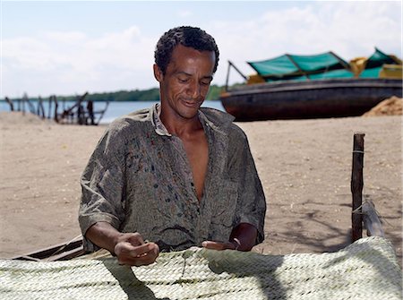 simsearch:862-03364303,k - A man stitches together woven strips of palm fronds to make a large floor mat at Matondoni,Lamu Island. The place has been famous for making traditional wooden sailing boats for a century or more. Foto de stock - Con derechos protegidos, Código: 862-03366610