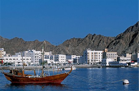 A wooden dhow moored in the harbour at Muttrah with the whitewashed apartment blocks and arid mountains behind Fotografie stock - Rights-Managed, Codice: 862-03360122