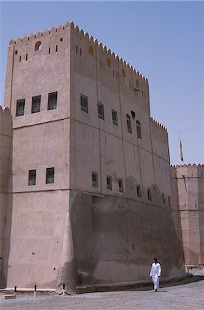 simsearch:862-03360228,k - An Omani man walks past the high sided living quarters of Barka Fort,a major landmark on the Batinah coast. Dating from the early Ya'ruba Period,it has an unusual octagonal tower and two restored watchtowers. Foto de stock - Direito Controlado, Número: 862-03360169