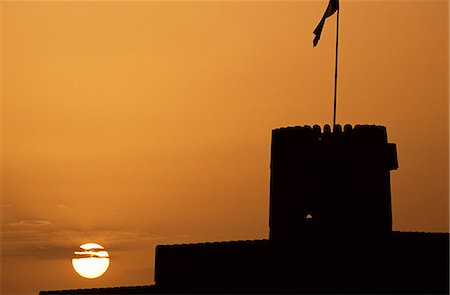 simsearch:862-03437387,k - Silhouette of one of the towers of Ras al Hadd Castle at sunset. The 450 year old castle stands looking out to sea. It has 3 towers and a courtyard large enough to take all of the villagers when they were threatened with invasion. An escape tunnel travels 200m outside the fort into what was then a dwelling. Fotografie stock - Rights-Managed, Codice: 862-03360204