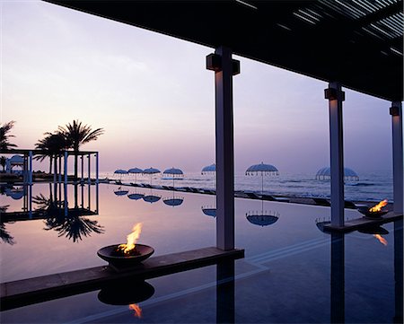 Palm trees,gas braziers,the shaded surround and the elegant poolside umbrellas are reflected in the still water of the infinity pool at sunset,at the Chedi Hotel Stock Photo - Rights-Managed, Code: 862-03360250