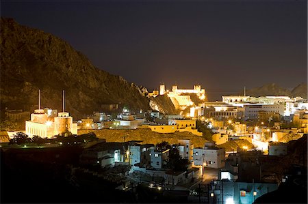 Oman,Muscat,Old Town. Fort Mirani illuminated by floodlights,built by the Portuguese in the 16th century,overlooks the old town.The sultan's palace,Al Alam,is on the right. Surrounding the town and visible on the left are chocolate brown ophiolites,a metamorphic igneous rock. Foto de stock - Con derechos protegidos, Código: 862-03360308