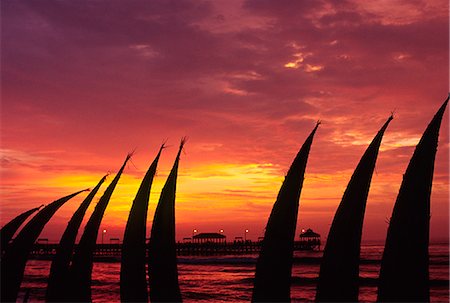 The setting sun paints the sky red,silhouetting totora (reed) boats stacked on the beachfront at Huanchaco,in northern Peru. The boats are the traditional craft of the local pescadores (fishermen). Stock Photo - Rights-Managed, Code: 862-03360562