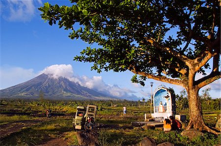 simsearch:862-03360828,k - Philippines,Luzon Island,Bicol Province,Mount Mayon (2462m). Near perfect volcano cone with a plume of smoke with grotto and motorcycle in a field. Foto de stock - Con derechos protegidos, Código: 862-03360777