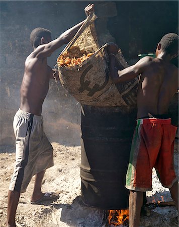 rum - Men tip sugar cane pulp into a drum for boiling with water as the first stage to making rum using a crude open-air still. Stock Photo - Rights-Managed, Code: 862-03363981