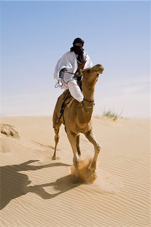 Mali,Timbuktu. In the desert north of Timbuktu,a Tuareg man rides his camel across a sand dune. He steers the animal with his feet. Stock Photo - Rights-Managed, Code: 862-03437232