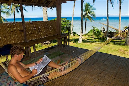 filipino - Philippines,Southern Leyte. Coral Cay Conservation volunteer relaxing in a hammock and studying dive plan charts. . Foto de stock - Con derechos protegidos, Código: 862-03437311