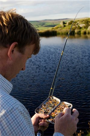 pesca con la mosca - UK,Wales,Conwy. A fisherman selects a fly from his fly-box whilst trout fishing in North Wales Fotografie stock - Rights-Managed, Codice: 862-03437820