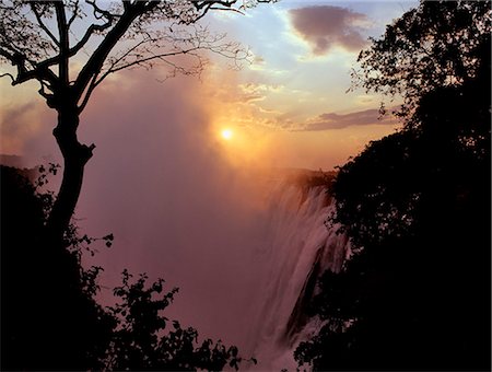 Sunset over the magnificent Victoria Falls. The Falls are more than a mile wide and are one of the world's greatest natural wonders. The mighty Zambezi River drops over 300 feet in a thunderous roar with clouds of spray. Foto de stock - Con derechos protegidos, Código: 862-03438064
