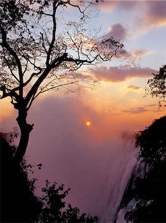 Sunset over the magnificent Victoria Falls. The Falls are more than a mile wide and are one of the world's greatest natural wonders. The mighty Zambezi River drops over 300 feet in a thunderous roar with clouds of spray. Foto de stock - Con derechos protegidos, Código: 862-03438065
