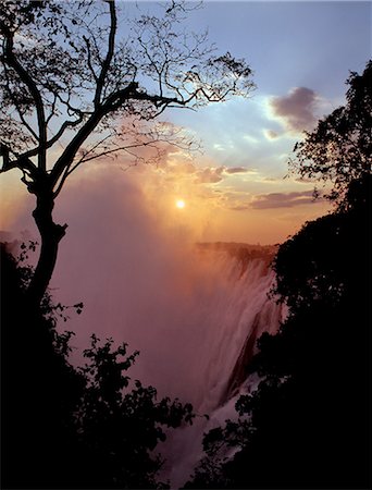 Sunset over the magnificent Victoria Falls. The Falls are more than a mile wide and are one of the world's greatest natural wonders. The mighty Zambezi River drops over 300 feet in a thunderous roar with clouds of spray. Foto de stock - Con derechos protegidos, Código: 862-03438063