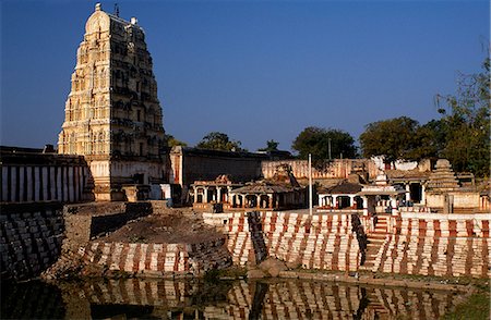 A soaring gateway and the painted steps of a water tank stand by the side entrance of the Virupaksha temple,Hampi's largest and still functioning temple Stock Photo - Rights-Managed, Code: 862-03711876