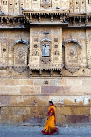 simsearch:862-06825838,k - Inde, Rajasthan, Jaisalmer. Sur les murs extérieurs de haveli plus grand de la ville, la rue vie continue comme d'habitude comme un sari femme vêtue marche aux côtés des murs très décorés. Photographie de stock - Rights-Managed, Code: 862-03712037