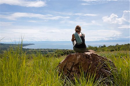 simsearch:862-06542513,k - Malawi, Lake Malawi. A tourist sits on a boulder, surrounded by grasses, looking out over Lake Malawi. Foto de stock - Con derechos protegidos, Código: 862-03712978