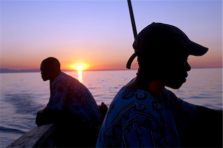Malawi, Lake Malawi; sunset over the lake with the head of local boatmen outlined by the setting sun. Foto de stock - Con derechos protegidos, Código: 862-03713010