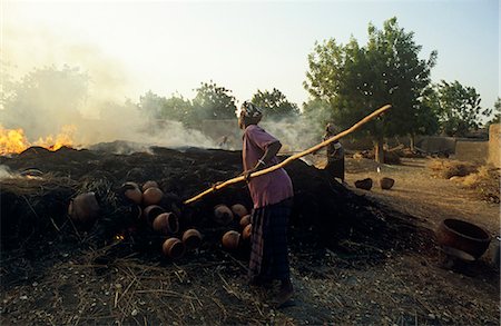 fornace - Mali, near Segou, Kalabougou. A woman rakes a fire in which pottery - for which this village is famous - is baked. Fotografie stock - Rights-Managed, Codice: 862-03736916