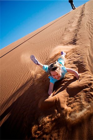 Sossusvlei, Namib-Naukluft National Park, Namibia. A young girl slides and tumbles down a sand dune in the Namib Desert. Stock Photo - Rights-Managed, Code: 862-03737010