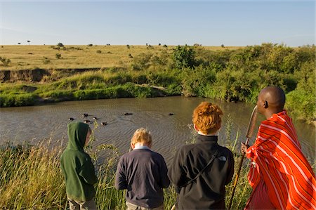 safaris - Kenya, Masai Mara.  Safari guide, Salaash Ole Morompi, leads boys to a vantage point overlooking a pod of hippos. Foto de stock - Con derechos protegidos, Código: 862-03731736