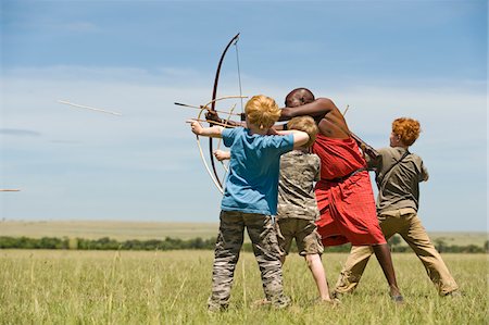 supervivencia - Kenya, Masai Mara.  Safari guide, Salaash Ole Morompi, teaches children archery Maasai style. Foto de stock - Con derechos protegidos, Código: 862-03731742