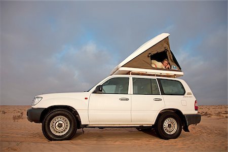 Oman, Wahiba Sands. A young lady peeps out from her roof-top tent early in the morning. Foto de stock - Direito Controlado, Número: 862-03808150