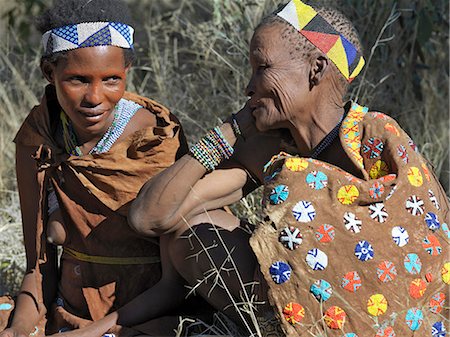 Deux femmes de la bande de rassembleur de chasseur NIIS parlent ensemble.La femme plus âgée porte une cape de cuir joliment décorées.Ils vivent dans l'environnement hostile d'une vaste étendue de sable plat et bush gommage pays cheval sur la frontière de la Namibie Botswana. Photographie de stock - Rights-Managed, Code: 862-03820242