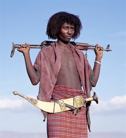 Warriors of the nomadic Afar tribe wear their hair long and carry large curved daggers, known as jile, strapped to their waists.Proud and fiercely independent, they live in the low lying deserts of Eastern Ethiopia.Modern rifles have now replaced daggers as weapons although most young men still wear ornate daggers by tradition. Fotografie stock - Rights-Managed, Codice: 862-03820404