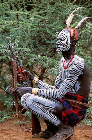 person with a rifle - An elder of the Karo tribe, a small Omotic tribe related to the Hamar, who live along the banks of the Omo River in southwestern Ethiopia. The Karo are renowned for their elaborate body painting using white chalk, crushed rock and other natural pigments. This man also has a clay hairdo typical of tribal elders. Stock Photo - Rights-Managed, Code: 862-03820419