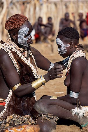 A Karo woman paints her daughters face with white chalk. The mother has styled her hair with mud and ochre. She wears a calfskin cape edged with cowrie shells, and layers of beads, bracelets and amulets. A small Omotic tribe related to the Hamar, who live along the banks of the Omo River in southwestern Ethiopia. Stock Photo - Rights-Managed, Code: 862-03820422