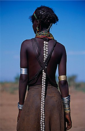 Éthiopie, Omo que jeune fille Dassanetchs porte ses cheveux partiellement tressé et enduit en ocre et de graisse animale. Typique de sa tribu, elle a une jupe en cuir, des bracelets métalliques et des amulettes et des couches de colliers de perles. Une lanière de cuir longue décorée de cauris se bloque vers le bas de son dos. Beaucoup la plus grande des tribus dans la vallée de l'Omo numérotation environ 50 000, les Dassanetchs, également connu sous le nom de la g Photographie de stock - Rights-Managed, Code: 862-03820435