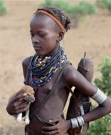 ethiopie - An attractive Dassanech girl holds a puppy.Her adornment is typical of the girls of her tribe.Since the Omo Delta is one of the least accessible and least developed parts of East Africa the culture, social organization, customs and values of the people have changed less than elsewhere. Foto de stock - Con derechos protegidos, Código: 862-03820447