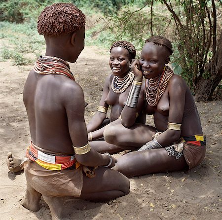 Karo girls chat in the shade of the riverine forest that lines the banks of the Omo River. It is a tradition for girls to pierce a hole below the lower lip in which they place a thin piece of metal or a nail for decoration.The Karo are a small tribe living in three main villages along the lower reaches of the Omo River in southwest Ethiopia. Foto de stock - Direito Controlado, Número: 862-03820449
