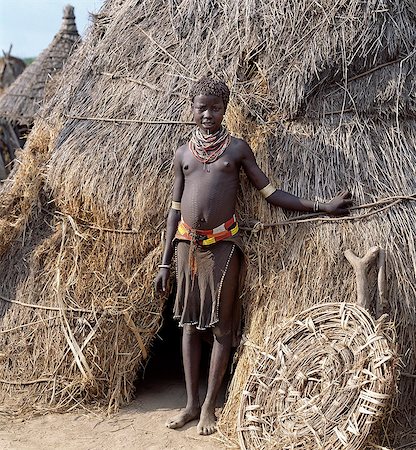 simsearch:862-03820457,k - A Karo girl in traditional attire stands outside her familys home.The door of the low entrance to the house is propped against its thatched wall.Most girls pierce a hole below the lower lip in which they place a thin piece of metal or a nail for decoration.The Karo are a small tribe living in three main villages along the lower reaches of the Omo River in southwest Ethiopia. Stock Photo - Rights-Managed, Code: 862-03820457