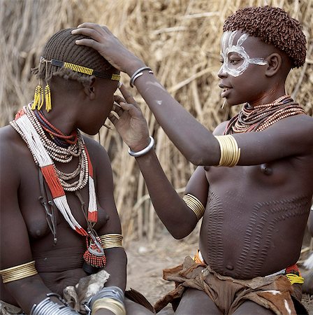 simsearch:862-03820457,k - Karo girls paint their faces in preparation for a dance. It is a tradition for girls to pierce a hole below the lower lip in which they place a thin piece of metal or a nail for decoration. Elaborate scarification is not an unusual form of body decoration.The Karo are a small tribe living in three main villages along the lower reaches of the Omo River in southwest Ethiopia. Stock Photo - Rights-Managed, Code: 862-03820452