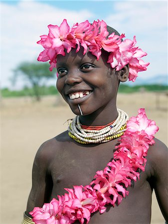 A young Kwegu girl garlanded with wild Desert Rose flowers.Adopting the practice of Karo women and girls, many Kwegu girls pierce a hole below the lower lip in which they place a thin piece of metal or a nail for decoration.The Kwegu known to the Karo as Muguji, a degoratory name meaning Working Ant, are the smallest tribe living on the banks the Omo River in southwest Ethiopia. Stock Photo - Rights-Managed, Code: 862-03820506