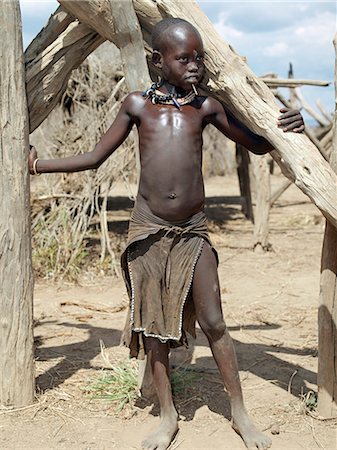 simsearch:862-03820417,k - Une jeune fille de Kwegu se trouve entre les poteaux de bois sec à la maison de sa famille.Adopter la pratique de Karo femmes et filles, beaucoup de filles Kwegu percer un trou en dessous de la lèvre inférieure dans laquelle ils placent un mince morceau de métal ou un clou pour la décoration.La Kwegu sait le Karo comme Muguji, un nom degoratory, qui signifie travail Ant, la plus petite tribu vivent sur les rives du fleuve Omo en Éthiopie. Photographie de stock - Rights-Managed, Code: 862-03820507