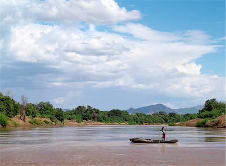 simsearch:862-03711647,k - A Karo man poles a dugout canoe across the Omo River. The Mursi Hills rise in the background.The Karo are a small tribe living in three main villages along the lower reaches of the Omo River in southwest Ethiopia. Foto de stock - Con derechos protegidos, Código: 862-03820501