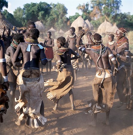A lively Nyangatom dance is enjoyed by villagers in the late afternoon.The elevated houses in the background are both homes and granaries, which have been built to withstand flooding when the Omo River bursts its banks The Nyangatom are one of the largest tribes and arguably the most warlike people living along the Omo River in Southwest Ethiopia. Stock Photo - Rights-Managed, Code: 862-03820558