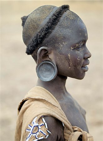 The typical hairstyle of a young Mursi girl.The Mursi speak a Nilotic language and have affinities with the Shilluk and Anuak of eastern Sudan.They live in a remote area of southwest Ethiopia along the Omo River, the countrys largest river. Stock Photo - Rights-Managed, Code: 862-03820568